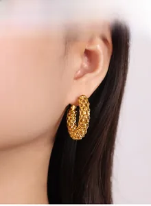 Gros plan de boucles d'oreilles créoles dorées à texture tressée portées par un mannequin