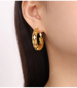 Détail de boucles d'oreilles en acier titane doré avec motif texturé portées par un mannequin