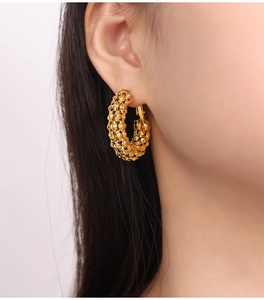 Gros plan de boucles d'oreilles créoles dorées forme C avec texture perlée en 3D