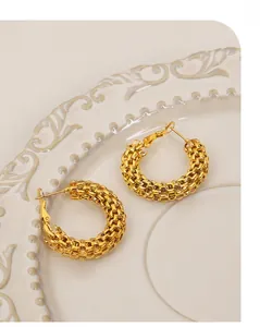 Gros plan de boucles d'oreilles créoles dorées en C avec texture maillée tressée