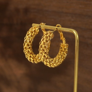 Boucles d'oreilles créoles dorées avec texture tissée sur un présentoir minimaliste
