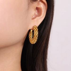 Boucles d'oreilles créoles dorées en acier titane avec texture gaufrée portées par modèle