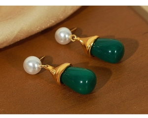 Detail of elegant gold-plated earrings with white pearl and green teardrop resin charms