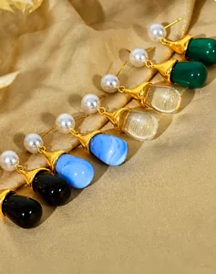 Detailed view of teardrop pearl earrings in four colors on elegant gold silk fabric