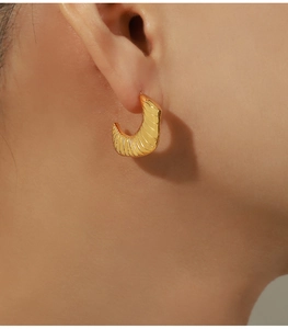 Detailed close-up of a gold-plated horn-shaped earring with spiral textured engraving