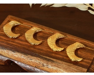 Detailed view of gold plated croissant and honeycomb textured earrings on a wooden stand