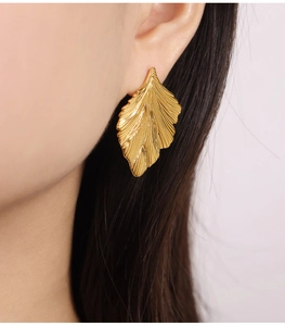 Macro shot of gold-plated ginkgo leaf earrings with brushed matte texture on model