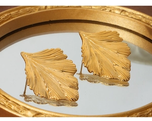 Detailed close-up of gold leaf earrings with intricate vein textures on a mirror surface