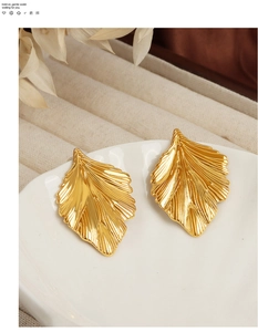 Detailed view of gold-plated leaf earrings with delicate radial vein texture on white tray