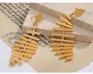 Detail of long gold tassel earrings with a geometric fishbone design on a stone texture