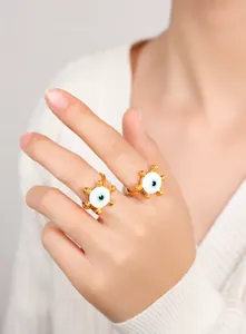 Nahaufnahme vergoldeter Evil-Eye-Ringe mit weißer Emaille und blauen Pupillen an der Hand