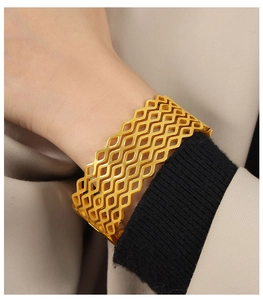 Primer plano de un brazalete geométrico calado de oro sobre una manga negra