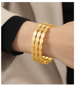Primer plano de brazalete ancho dorado con patrón geométrico de nido de abeja en la muñeca