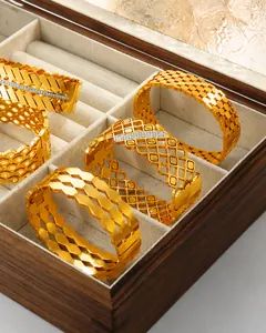 Vista detallada de brazaletes geométricos bañados en oro con pedrería en joyero de madera