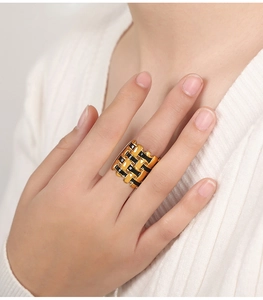 Detail of a wide gold woven ring with black enamel texture worn on middle finger
