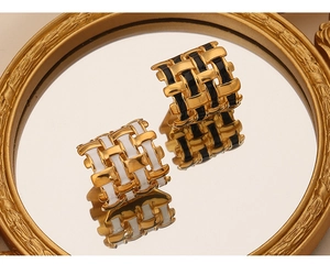 Detail view of square woven earrings with black and white enamel on a mirror reflection