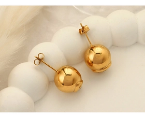 Détail de boucles d'oreilles boules dorées sur plateau en céramique blanche