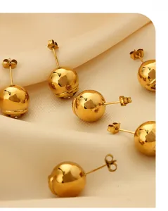 Détail de six boucles d'oreilles boules dorées polies sur un tissu en soie blanche