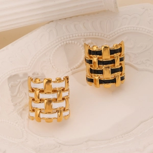Gold-plated braided rings with black and white enamel finish on a white ceramic tray