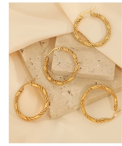 Close-up of gold twisted hoop earrings on beige travertine stone with satin fabric