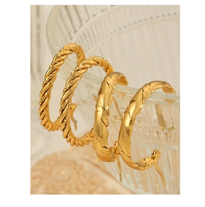 Detail of gold twisted rope and wide diagonal ribbed earrings on glass rim