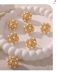Macro detail of gold-plated woven earrings with inlaid pearls on a textured tray