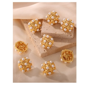 Close-up of vintage gold woven earrings with inlaid pearls on a textured stone surface