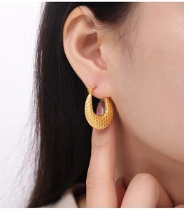 Primer plano de pendientes dorados en forma de U con patrón de panal en una modelo mujer