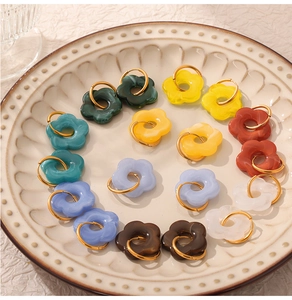 Detailed macro view of colorful resin five-petal flower hoop earrings on a ceramic plate