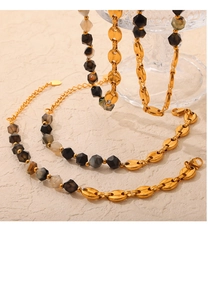 Detailed shot of 18K gold-plated mariner link chains and beaded necklaces on a stone surface