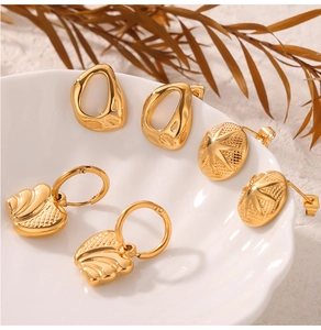 Détails de trois boucles d'oreilles géométriques plaquées or 18 carats sur une assiette blanche