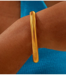 Detail of a wide gold-plated stainless steel flexible cuff bracelet with a ribbed texture