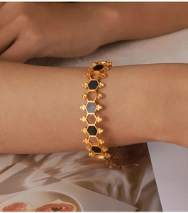 Dettaglio del bracciale a nido d'ape dorato con inserti neri indossato su un polso