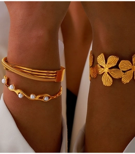 Detail of gold-plated titanium steel floral bangle and layered pearl bracelet on model