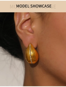 Macro shot of gold teardrop earrings featuring vertical stripes and white zircon inlay