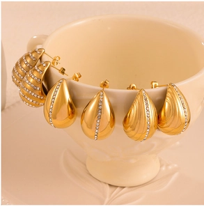 Close-up of gold-plated teardrop earrings with zircon accents on a ceramic cup