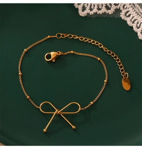 Detail van een 18K vergulde strikarmband met fijne kralenketting op een donkergroen dienblad