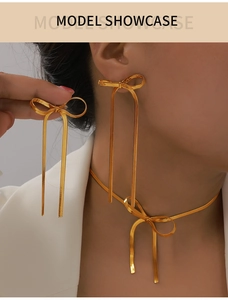 Dettaglio di orecchini a fiocco dorati e collana con lunghe nappe e trama a catena di serpente