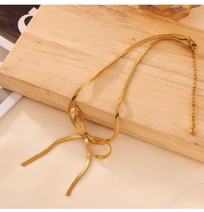Dettaglio della collana a fiocco placcata oro 18K con catena a serpente su legno
