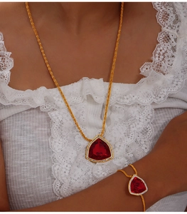 Detail der roten Dreieck-Halskette und Goldkette auf einer weißen Spitzenbluse