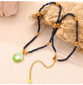 Detail of natural stone beaded necklace with enamel pendant and S.Steel tag on sand