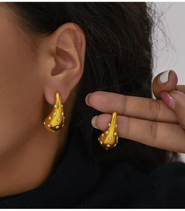 Detail of gold teardrop earrings with white crystals on a 18K gold plated metal surface