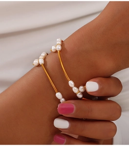Detalle de brazaletes minimalistas de titanio chapados en oro con perlas barrocas en la muñeca