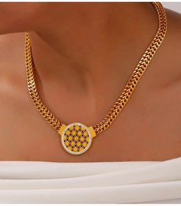 Détail d'un pendentif géométrique doré sur une grosse chaîne en épi portée par un mannequin