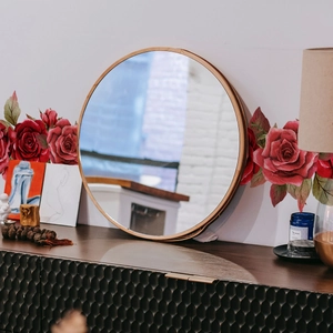 Round rose gold mirror with slim metal frame on a dark textured cabinet with roses
