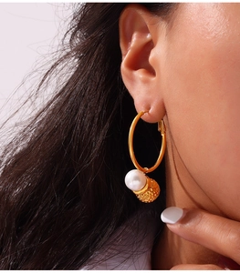 Close-up of golden hoop earrings featuring a white pearl and a textured hammered metal ball