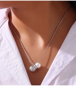 Detailed close-up of a hammer-textured silver ball and pearl pendant on a snake chain