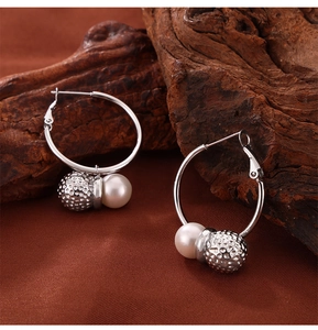 Close-up of silver-tone hammered metal ball and white pearl charms on hoop earrings