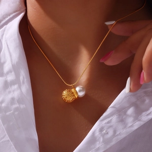 Gold snake chain necklace featuring a white pearl and a hammered gold orb pendant on model