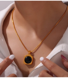 Gros plan d'un collier chaîne serpent dorée avec un pendentif carré en pierre noire